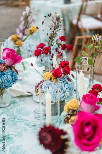 Space prepared to a event with chairs and table with flower for decoration. There is a rail with more decoration flowers and candle.