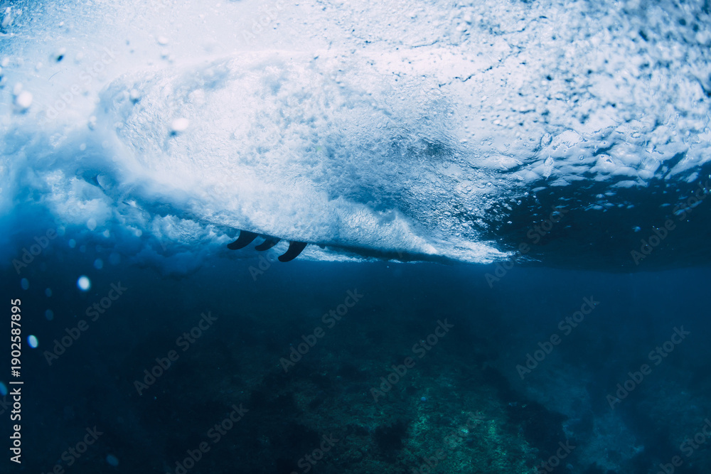 Obraz premium Underwater view of surfer rides wave with surfboard, deep blue ocean energy and extreme water sports concept.