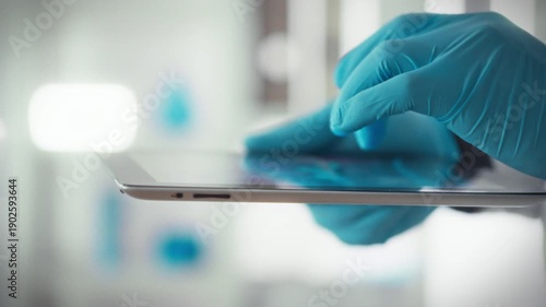 Healthcare workers wearing nitrile gloves operate a digital tablet to access a healthcare database and update patient records, an example of effective professional medical practice