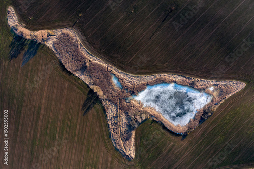 Abstract Aerial View of Frozen Pond Surrounded by Agricultural Fields