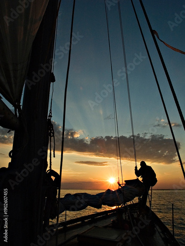 crew member working on the sail of a large traditional sailing vessel at sunset