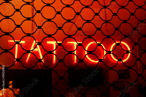 Quadro su tela Red neon Tattoo sign behind iron metal bars at night.