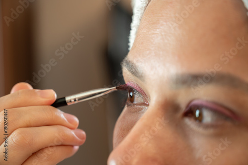 Woman blending eyeshadow with a makeup brush on her face.
Beauty and skincare routine concept. Professional makeup application, cosmetics, self-care, and personal grooming. Close-up portrait.