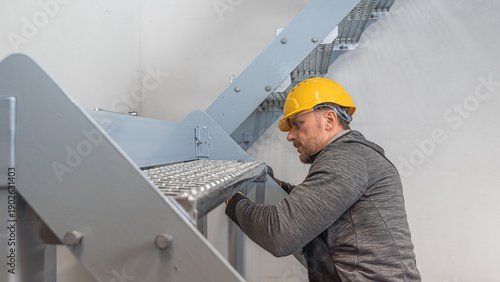 Assembly of prefabricated steel staircase. Worker connects a steel beams and steel step of stair using a screw connection