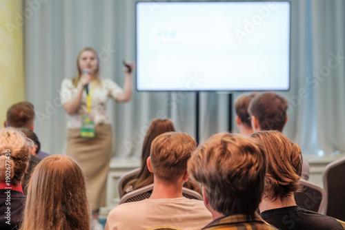 Presenter speaks to attentive audience during conference with large screen