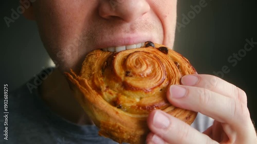 Close up man mouth eating delicious freshly baked sweet bun. He eagerly bites into pastry, chews it with pleasure, enjoying his breakfast or sweet snack during day. Man eating sweet pastry bun