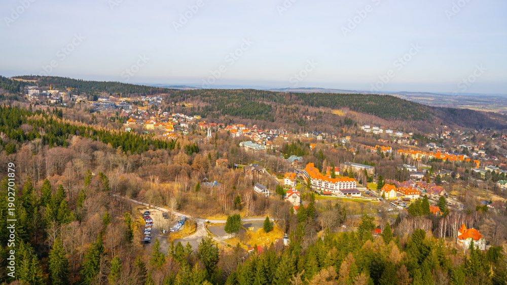 Fototapeta premium A town is seen from above with buildings and roads. Trees cover the hills in the distance. The scene shows a clear sky and an open landscape. People live and work in this area.