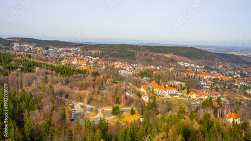 A town is seen from above with buildings and roads. Trees cover the hills in the distance. The scene shows a clear sky and an open landscape. People live and work in this area.
