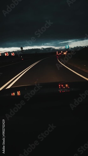 Vertical video of a car driving along a winding highway at dusk in Poland. Visible road signs and headlights of oncoming traffic under a dark cloudy sky.