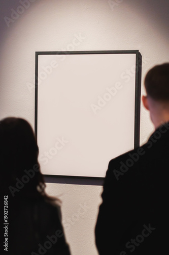 Visitors look at an empty art frame in a gallery during an exhibition at a local art center in the evening