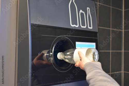Fotografie A woman hands over plastic bottles to a recycling machine.