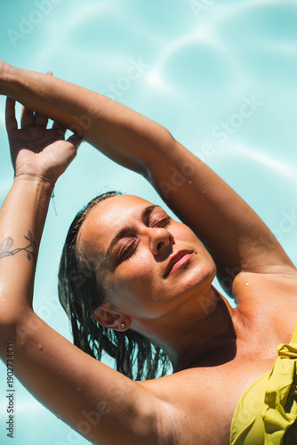 Fotografie Young woman relaxing by the swimming pool in bright sunlight, dreaming and sunba
