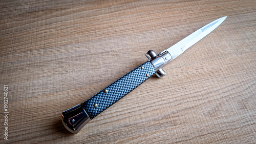 Folding knife with textured handle placed on a wooden surface. Close-up of a pocket knife showing metal blade, craftsmanship, and everyday carry concept.
