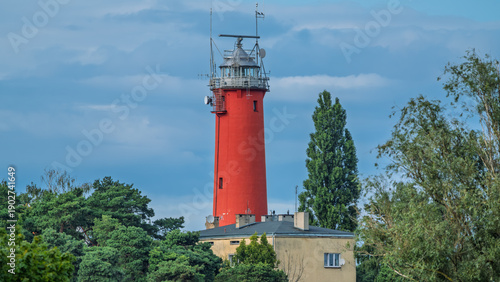 Bright red lighthouse tower above green trees