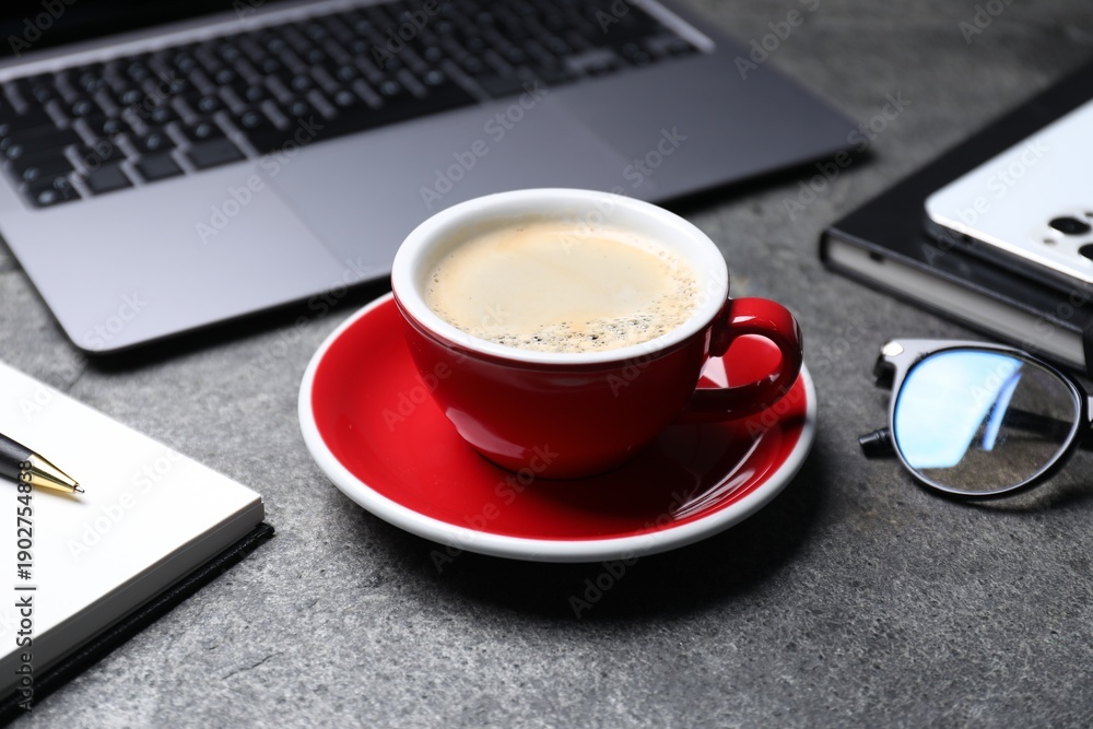 Naklejka premium Cup of aromatic coffee, laptop and office essentials on grey table, closeup