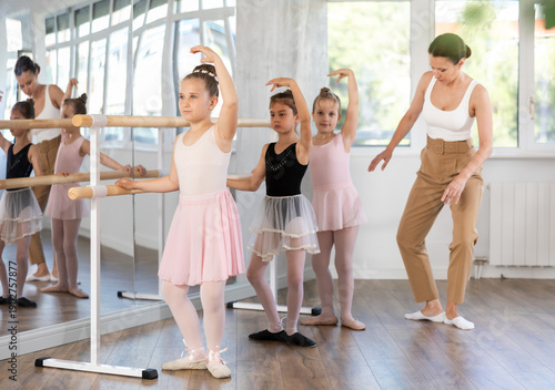 Fotografie Adult woman teacher helping group of girls dancers practicing plie movement at b