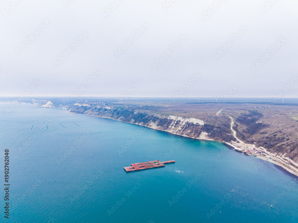Obraz premium Cement platform in the sea with coastline view near wind turbines and cliffs on an overcast day
