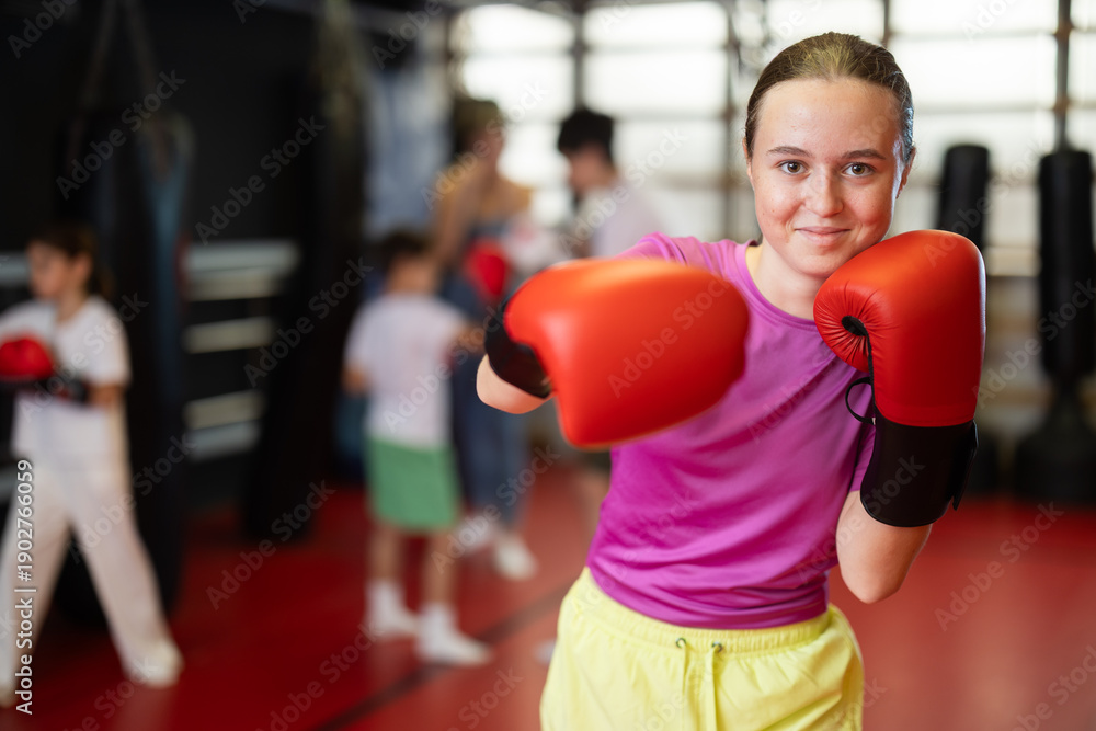 Obraz premium Teenage girl in red boxing gloves at training in the gym. Portrait of a boxing teenager. Muay Thai training for children