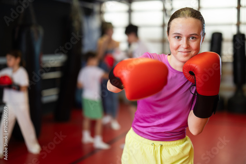 Teenage girl in red boxing gloves at training in the gym. Portrait of a boxing teenager. Muay Thai training for children