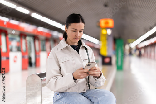 Woman monitors navigation of train in smartphone sitting on a bench at the metro station
