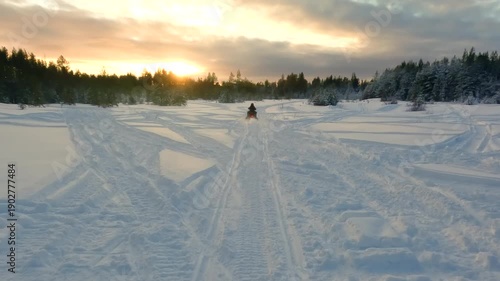 Point of view shot following a person riding a snowmobile through a beautiful winter landscape in Sweden, with the sun setting behind a snow covered pine forest, real sound