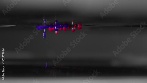 4K macro footage of red and blue ink drops falling from a UV printer's print head. Close-up of the modern printing process and technology.