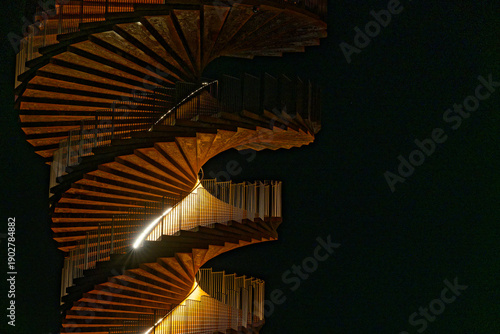 Spiral stairway rising upward against dark sky in silhouette.