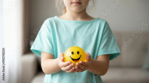 A young girl in a blue shirt holding a yellow smiley face stress ball