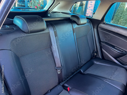 Car interior shows backseat space with black fabric and cushions while parked in a residential area during daylight