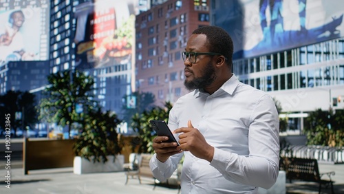 Bilde på lerret Black man navigating on mobile phone apps and walking the busy metropolitan street, urban roadway downtown with skyscrapers