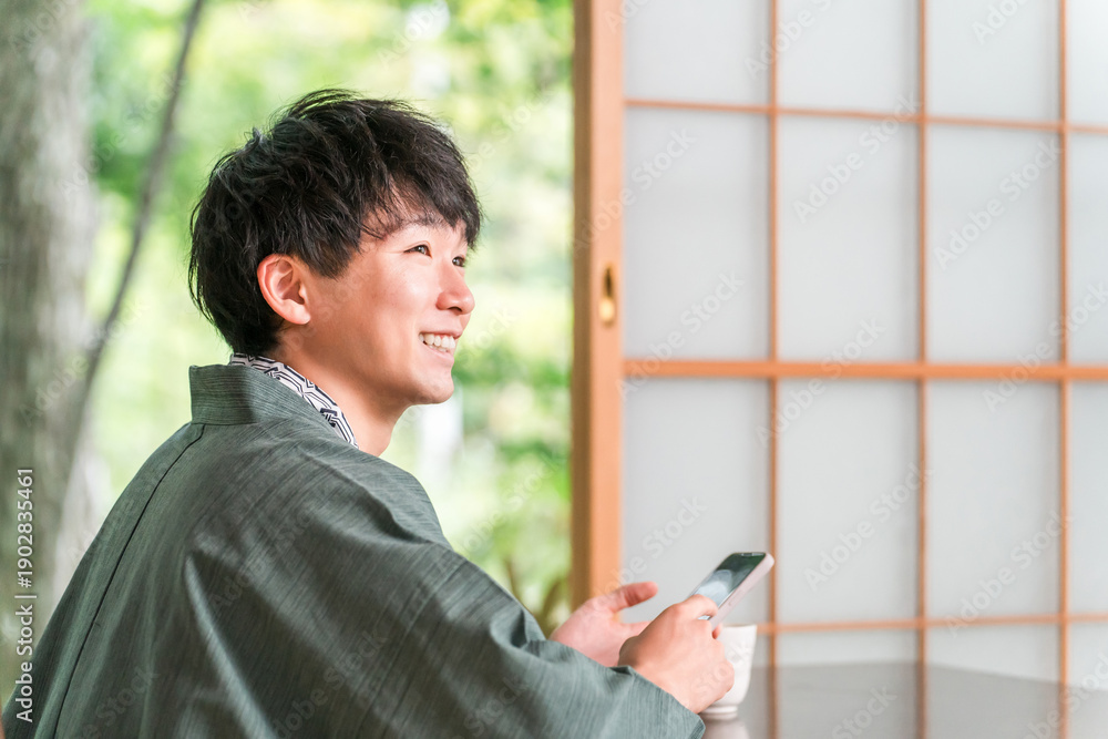 Obraz premium A man in a yukata looking at his smartphone in a Japanese-style room at a ryokan