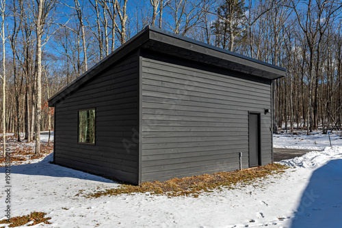 Modern minimalist outbuilding with slanted roof in winter forest setting