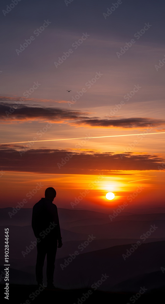 Fototapeta premium Man Silhouette Contemplating Dramatic Sunset Over Mountain Landscape
