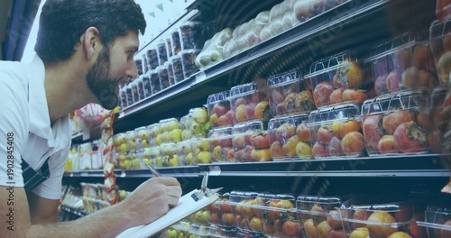 Schilderij op canvas Leaning man in white polo stripe checking peaches in produce, noting clipboard a
