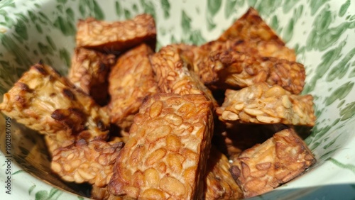 Foto Crispy fried tempeh in a traditional vintage enamel bowl under natural sunlight