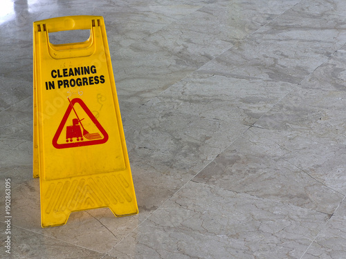 Minimal interior scene showing a yellow Cleaning in Progress caution sign placed on a marble tile floor, photographed from above with ample copy space and soft indoor lighting.