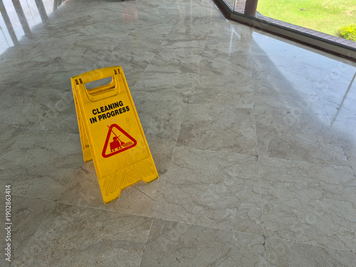 Minimal interior scene showing a yellow Cleaning in Progress caution sign placed on a marble tile floor, photographed from above with ample copy space and soft indoor lighting.