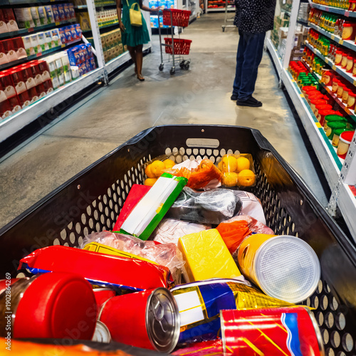 Point-of-view shot from inside a full grocery cart in a supermarket aisle