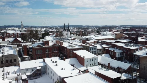 Aerial view of snow covered rooftops and historic church spires in a small town during winter.