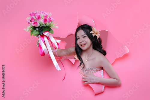 Lovely surprise for Valentine's: Elegant woman with a bouquet of pink roses breaking through pink paper wall.