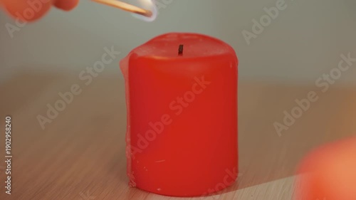 hand striking match to candle, closeup sequence of match ignition and flame catching red pillar wick on wooden table, careful deliberate motion suggests home ritual, aromatherapy setup or prelude
