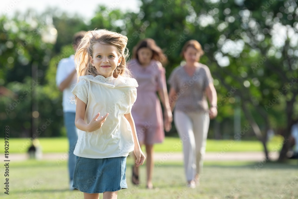 Obraz premium Happiness young girl smiling and running freely expressive outdoors cheerful child in motion with family blur background in nature. Closeup portrait of joyful daughter running with parents in park.