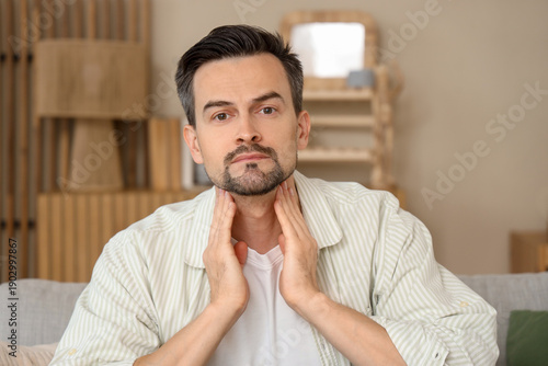 Handsome man self-examining thyroid gland at home
