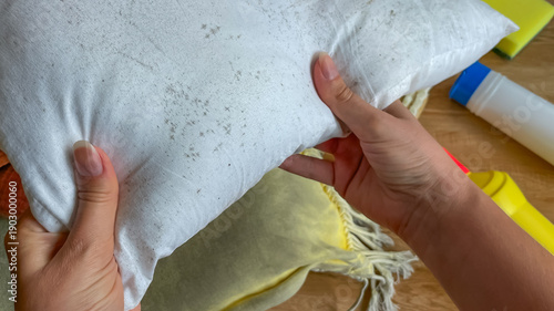 Hands holding a pillow with mold stains before cleaning. Concept for home cleaning, hygiene, textile care, and mold control.