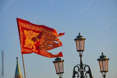 The flag of Venice with a lighthouse and blue sky in the background