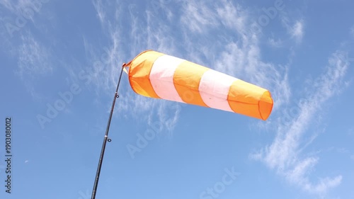orange and white striped windsock indicating wind direction on pole against a clear blue sky with light clouds, concept of weather monitoring, aviation, airfield safety