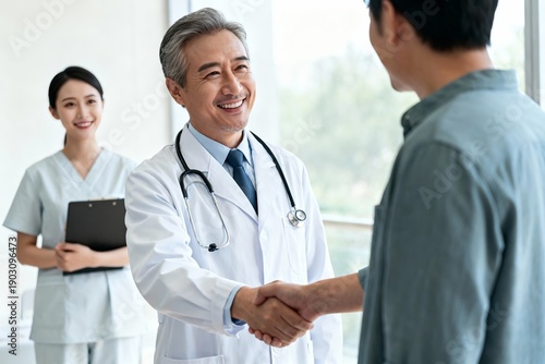 A doctor in a white coat shakes hands with a patient in a clinic. A nurse stands in the background holding a clipboard.