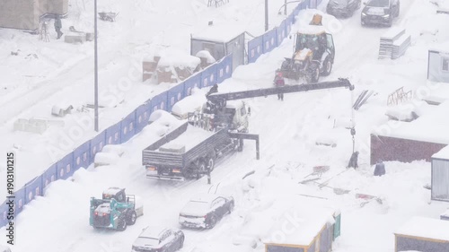 Truck mounted crane working on a construction site during heavy snowfall, winter construction work, loading materials, industrial machinery and cold weather conditions concept