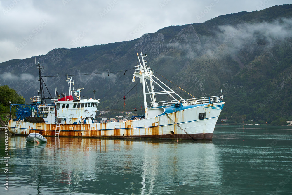 Naklejka premium Fishing boat anchored in harbor with mountain backdrop