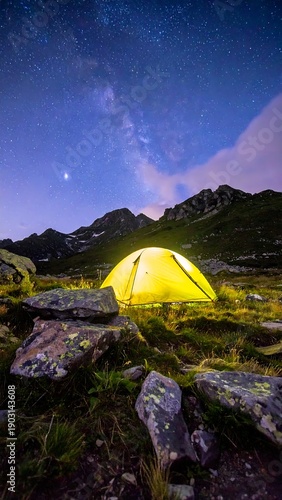 A glowing tent under the starry sky at mountain base surrounded by rocks